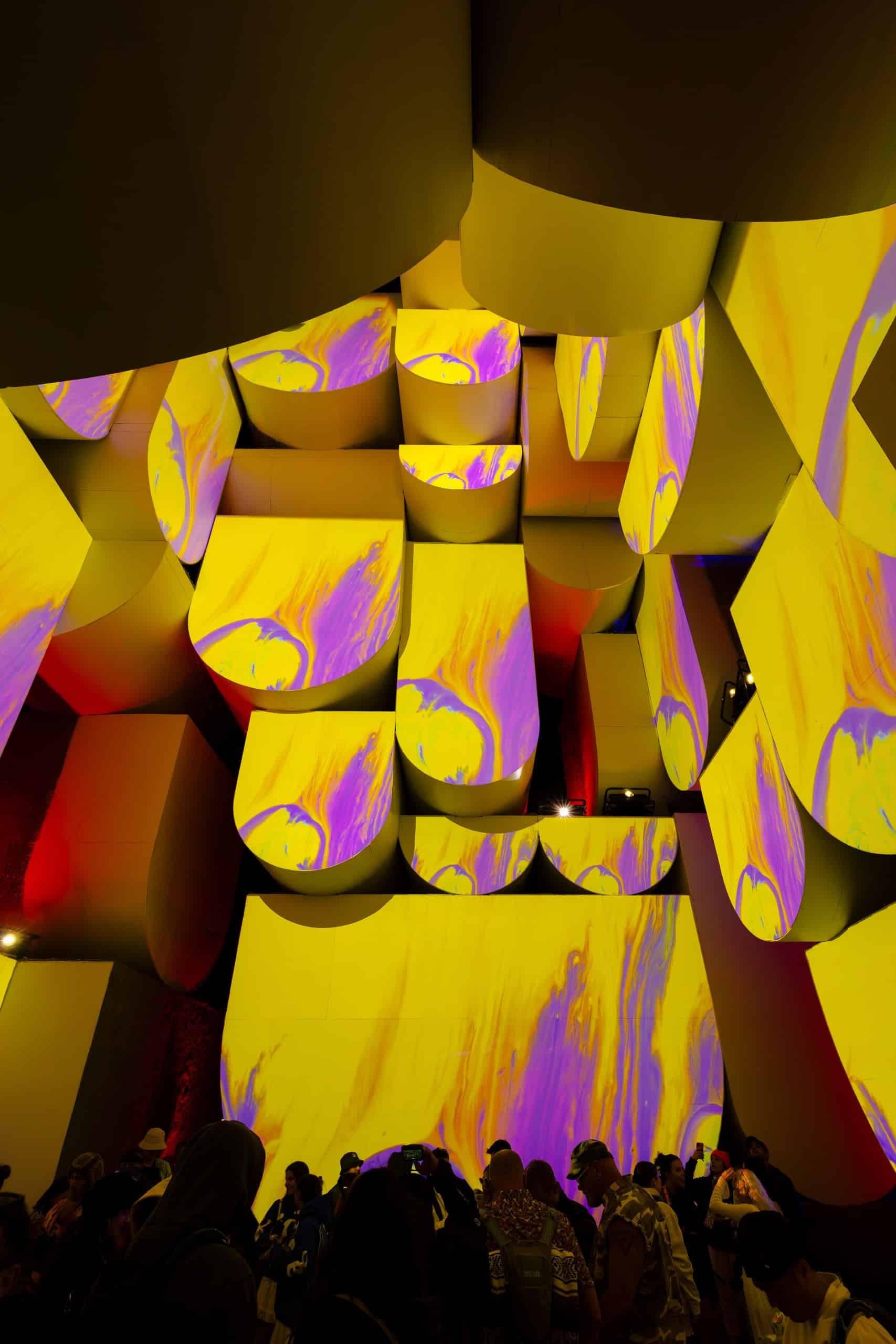 Das Innere einer Kunstinstallation, ein nach oben hin sich verjüngender Turm aus halbrunden Elementen, auf dessen Wände Projektionen in Gelb und Lila gestrahlt werden. Coachella 2024, Nebbia, Babylon, Foto: Lance Gerber