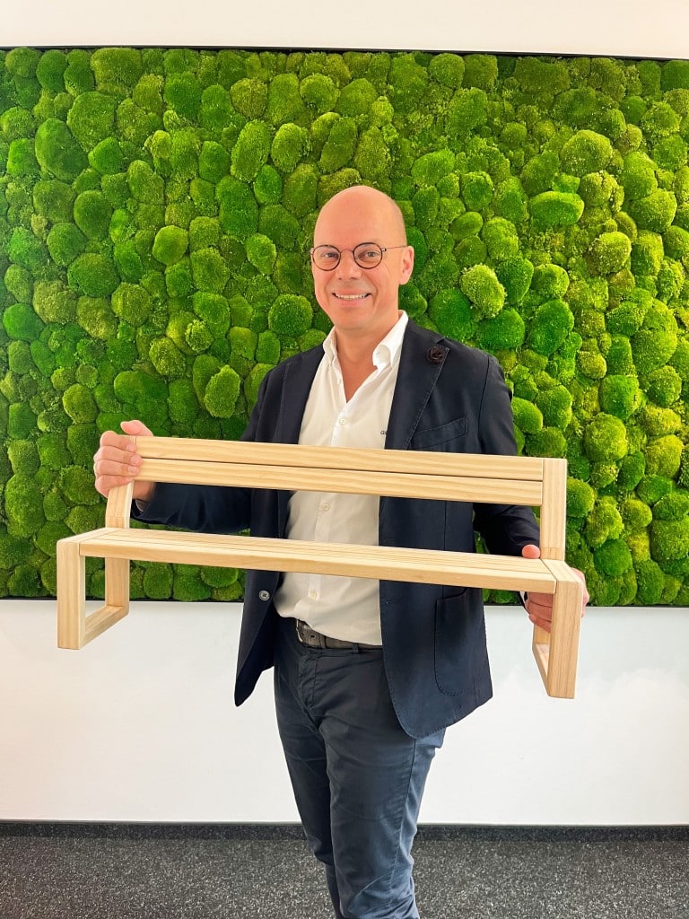 Ein Mann hält ein Modell eine Bank aus Holz, im Hintergrund ein Moosbild an der Wand. Oliver Runge, Geschäftsführender Gesellschafter der Runge GmbH & Co. KG Foto: Runge GmbH & Co. KG